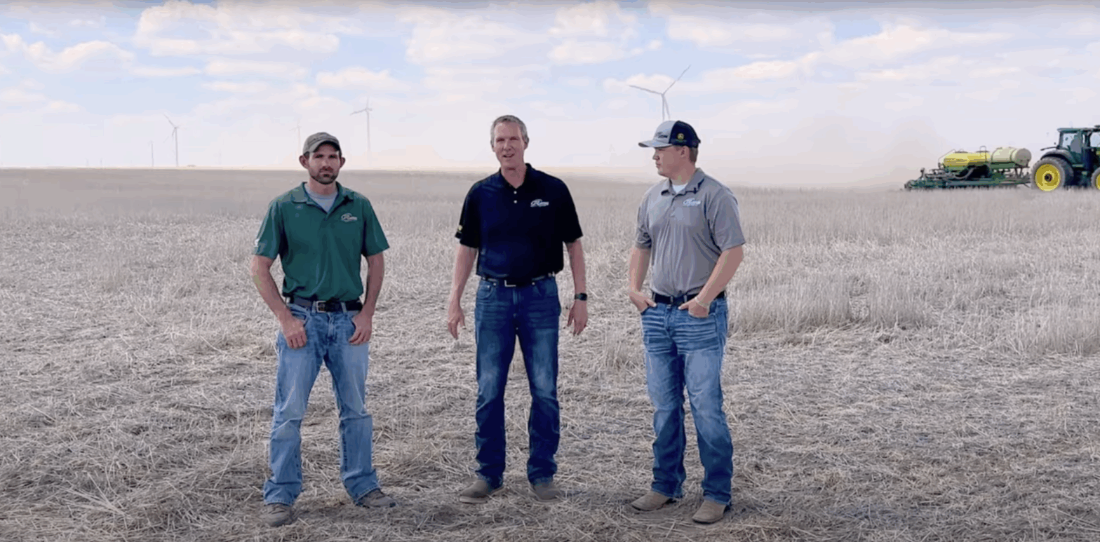 21st Century Precision Ag Team in field with large wind turbines in distance.